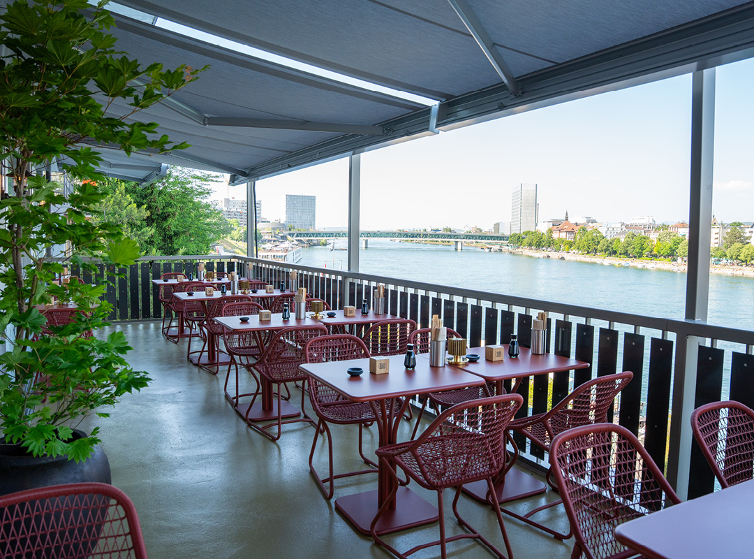 Negishi Basel Johanniterbrücke, bequeme Terrasse mit Rheinblick und viel Schatten, überdachte Aussensitzplätze für gemütliche Sommerstunden.